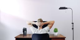 Person sitting at desk with hands behind head